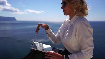 digital nómada, negocio mujer trabajando en ordenador portátil por el mar. bonito dama mecanografía en computadora por el mar a atardecer, hace un negocio transacción en línea desde un distancia. Lanza libre, remoto trabajo en vacaciones video