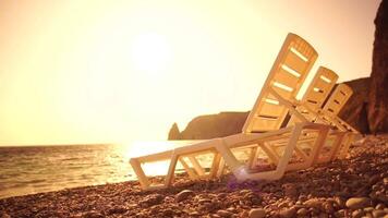 Rows of empty white plastic chair and sunbathing beds on beach near sea at sunset. Relaxation area for chilling out on summer. Beach Chairs and sun loungers outdoors. Summer Vacation resort concept. video