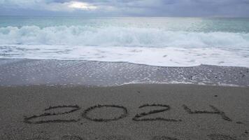 Happy New Year 2025 hand written digit 2024 washed by wave on the sea beach. Abstract background of coming New Year 2025 and leaving year of 2024. video