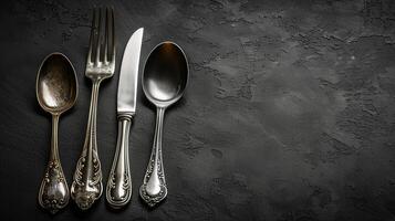 AI generated Vintage silverware set with ornate patterns, featuring a spoon, fork, knife, and teaspoon on a dark textured background, ideal for dining concepts or culinary presentations photo