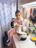 Budva, Montenegro - 13 august 2023. Little girl with a glass of milk in her hands sits on a table near the scales photo