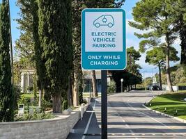 Budva, Montenegro - 17 august 2023. Sign with the inscription and the symbol of the car on a pole by the road in the park. Caption. Electric vehicle parking. Only while charging photo
