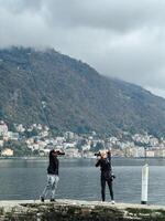 como, Italia - 12 noviembre 2023. fotógrafos con grande cámaras estar opuesto cada otro en el muelle y tomar imágenes de el mar y montañas foto