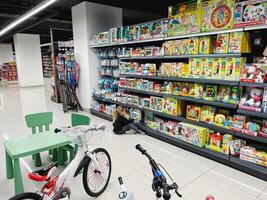 Budva, Montenegro - 01 december 2023. Little girl chooses a toy on a store shelf sitting on the floor photo