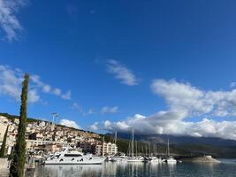 Sailing yachts stand near the shore with colorful houses in Lustica Bay. Montenegro photo