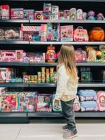 buda, montenegro - 18 agosto 2023. pequeño niña soportes en frente de estantería con muñecas en un supermercado foto