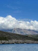 White cumulus clouds descend on a green mountain range by the sea photo