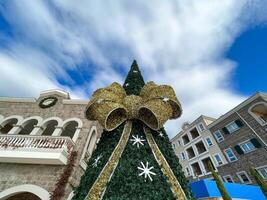 Artificial Christmas tree decorated with a huge golden bow stands in front of colorful houses photo