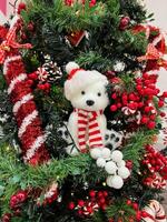 Small teddy bear sits on a Christmas tree decorated with garlands, balls and candies photo
