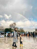 Mom with a little girl are standing near the market against the backdrop of a rainbow over the mountains photo