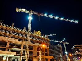 construcción grúas con iluminación terminado de muchos pisos edificios debajo construcción foto