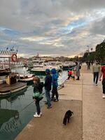 buda, montenegro - 25 diciembre 2022. niños y adultos estar en el muelle y Mira a el amarrado yates foto