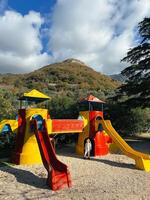 Little girl stands near a colorful playground with slides and towers photo