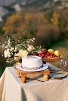 Boda pastel soportes en un estar en el mesa siguiente a un ramo de flores de flores y un plato de Fruta foto