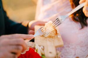 Bride and groom eat a wedding cake with forks from a wooden board. Cropped. Faceless photo