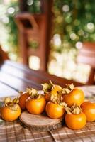 Ripe persimmon lies on a wooden board on a checkered napkin on a table in the garden photo