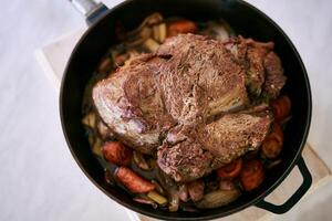 Juicy roast beef lies on stewed vegetables in a frying pan on the table. Top view photo