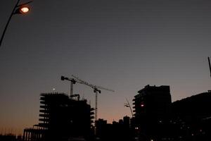 siluetas de torre grúas a el construcción sitio de Alto edificios a puesta de sol foto