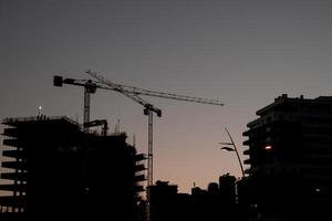 High tower cranes work on the construction site of high-rise buildings with illumination at sunset photo