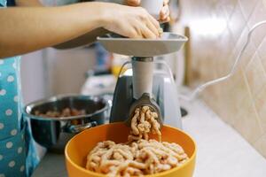 Cook twists minced meat on an electric meat grinder into a bowl on the table photo