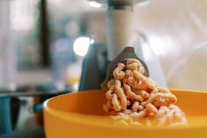 Fresh minced meat comes out of the electric meat grinder into a bowl photo