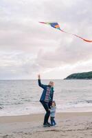 Little girl stands near a smiling mother with a kite in her hand near the sea photo