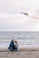 Mom is squatting looking at a kite, which is launched by a little girl on the seashore photo