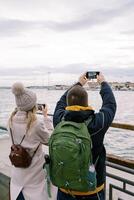 Man and woman shoot a port on the seashore with smartphones. Back view photo
