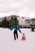 Smiling dad rides a small child on a sleigh on a snowy hill photo