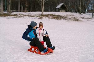 sonriente papá mirando a pequeño hija sentado en trineo en Nevado llanura foto