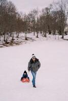 Dad carries a little boy on a sledge across a snowy plain near the forest photo