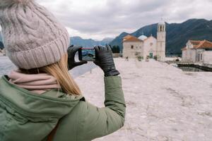 Young woman takes a picture of the Church of Our Lady on the Rocks with her smartphone. Back view. Montenegro photo