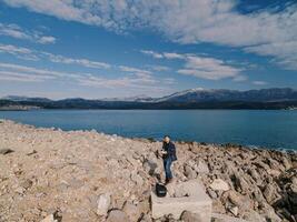 Operator with a drone remote control in his hands stands on a stone platform on a rocky seashore photo