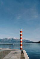 Small striped red and white lighthouse on a pier by the sea against the backdrop of mountains photo