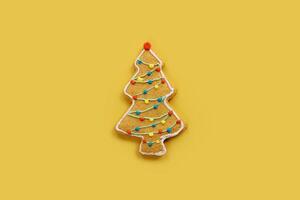 pan de jengibre Navidad árbol Galleta con guirnaldas de Formación de hielo en un amarillo antecedentes foto