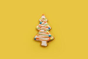 White glazed Christmas tree cookie with colorful garlands on a yellow background photo