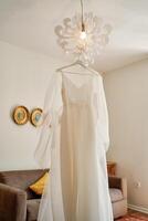 White bride dress hanging on a hanger on a chandelier in the room photo