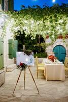 Wedding welcome sign on a tripod decorated with flowers near the set festive table photo