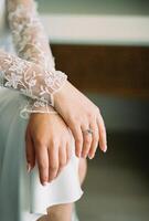 Bride in a white lace robe sits with her hands folded on her knees. Cropped. Faceless photo