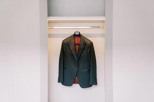 Groom black jacket hangs on a hanger in a white sliding wardrobe in the room photo
