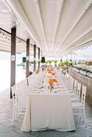 Long festive table set with bouquets of flowers under a canopy photo