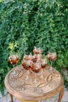 Glasses with red wine and floating grapes inside stand on a carved wooden table in the garden photo