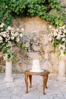 Wedding cake stands on a wooden table near a wedding semi-arch near a stone wall in the garden photo