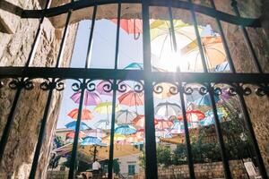 View through a wrought-iron fence to colorful umbrellas hanging above the street of an ancient town photo