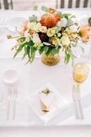 Bouquet of flowers stands on a festive table near an invitation with a paper heart on a napkin photo