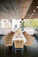 Long served table with bouquets of flowers and wicker chairs stands in a restaurant photo