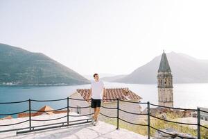 Smiling man leans on a rope fence on an observation deck near the church bell tower. Perast, Montenegro photo