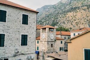 antiguo reloj torre entre Roca casas en el cuadrado. kotor, montenegro foto