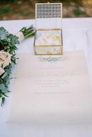 Wedding rings in a glass box stand on the marriage certificate on the table near the bouquet photo