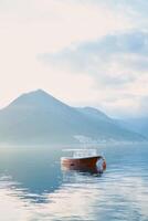 Moored boat in the sea against the backdrop of mountains in the fog in the evening photo